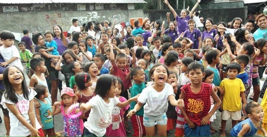 A crowd of children and Fishes & Loaves volunteers cheering with their arms raised at a community feeding day