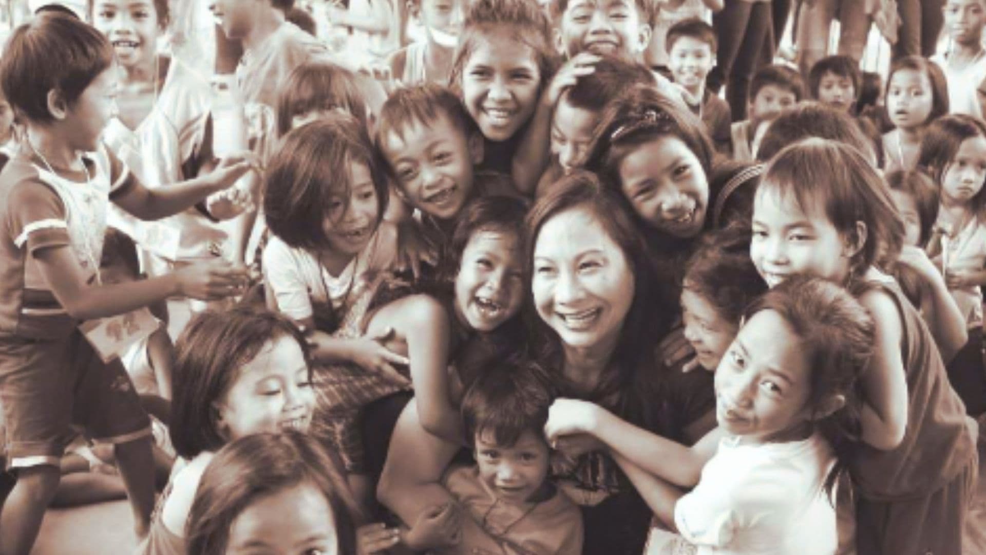 Children crowding around a Fishes & Loaves volunteer, all smiling and laughing